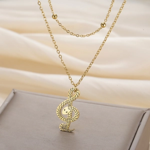 Detail van gouden dubbele ketting met slangenstructuur vioolsleutel hanger