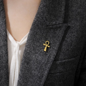 Detail of a golden Ankh cross brooch on a dark grey herringbone blazer lapel