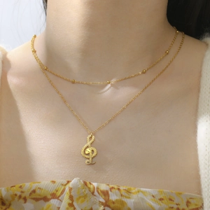 Detailopname van een dubbele goudkleurige ketting met een slang- en muzieksleutelhanger