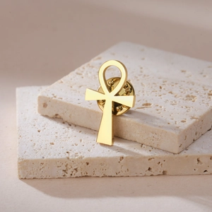 Polished gold Ankh cross brooch in 304 stainless steel displayed on beige stone boards
