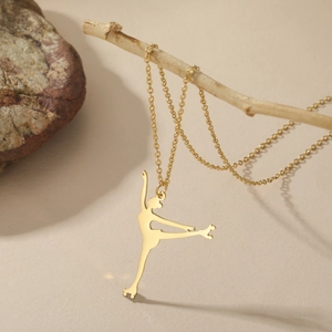 Detail eines goldenen Eiskunstläufer-Anhängers an einer Gliederkette auf Natursteinen