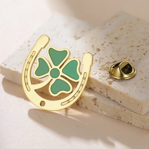 Detail of a golden four-leaf clover and horseshoe brooch with green enamel on stone base