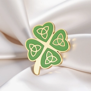 Detailed close-up of green clover brooch with golden triquetra knots on white silk fabric