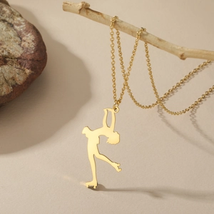 Detail eines goldenen Eiskunstläufer-Anhängers an einer Kette auf einem Naturzweig