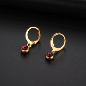Close-up of gold hoop earrings with deep red garnet birthstone charms on black surface