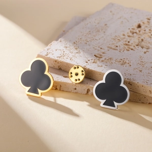 Broche de trébol de naipes en acero inoxidable negro y dorado sobre fondo de piedra