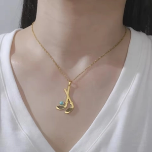 Detail of golf club pendant necklace in gold finish worn on a white V-neck shirt