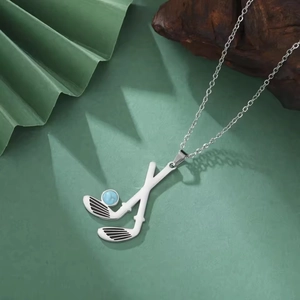Macro shot of stainless steel golf club pendant with blue bead on a green background