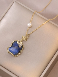 Dettaglio di una collana d'oro con pietra blu e perla su una scatola di gioielli in raso