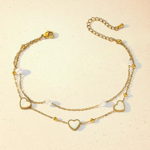 Close-up of double-layer gold anklet with heart pendants, pearls, and lobster clasp closure