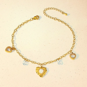 Detailed macro of gold heart and zircon charms on a delicate stainless steel anklet