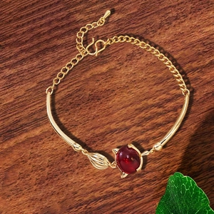 Details des Fuchs-Armbands in Gold mit rotem Edelstein und Blatt auf dunklem Holzgrund
