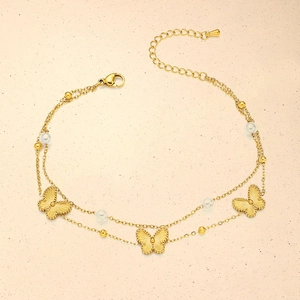 Close-up of double-layer gold anklet with butterfly charms and white pearls details