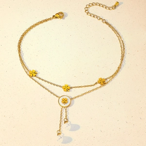 Detail of a double-layered gold anklet with clover charms and delicate white beads