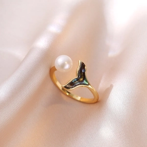 Dettaglio macro di un anello dorato aperto con perla e coda di pesce su seta