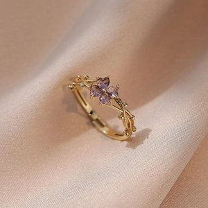 Dettaglio dell'anello d'oro con quattro pietre viola a cuore su seta color champagne