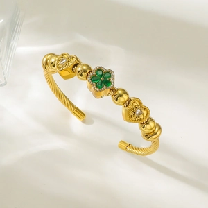 Détail du bracelet ouvert doré avec trèfle vert et breloques cœur sur tissu de soie
