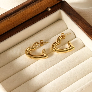 Détail de boucles d'oreilles cœur dorées polies dans un coffret à bijoux en velours beige