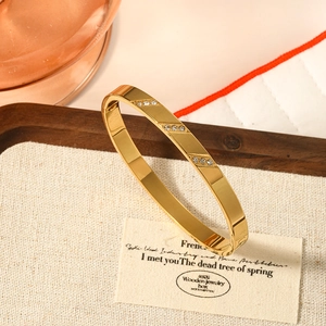 Elegant gold stainless steel bangle with inlaid stones on a textured display pad