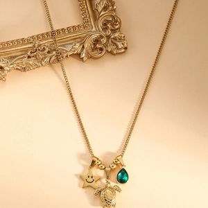 Détail du collier doré avec pendentif tortue, étoile souriante et gemme verte en goutte