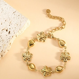 Golden stainless steel bracelet with smiling star and teardrop charms on a beige background