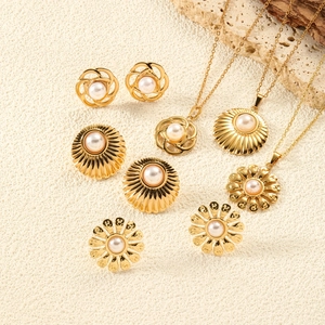 Golden heart jewelry set with pearls featuring floral designs on a textured stone background