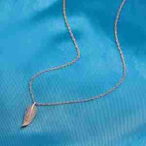 Gros plan d'un collier pendentif plume en acier titane sur un tissu en soie bleue