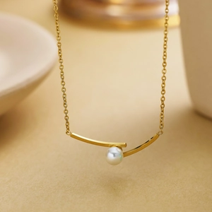 Macro detail of gold titanium necklace featuring a white pearl and irregular curved pendant