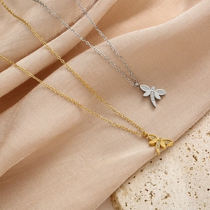 Detalle de colgantes de libélula en oro y plata con cristales sobre tela rosa suave