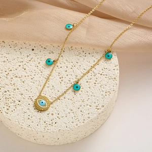 Detalle del collar de titanio dorado con dijes de ojo turco sobre expositor blanco