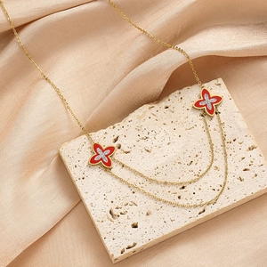 Detalle de collar dorado de doble capa con colgantes de trébol rojo y cristales finos