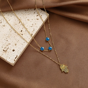Detail der zweilagigen Goldkette mit Hamsa-Hand-Anhänger und blauen Augenperlen