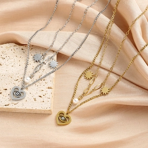 Detalle del collar multicapa de acero de titanio con corazón, ojo turco y perla