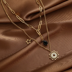 Detail einer goldenen mehrlagigen Halskette mit Sonnenanhänger und schwarzem Tropfen