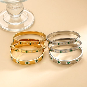 Gold and silver titanium bracelets with green emeralds and pavé crystals on orange background