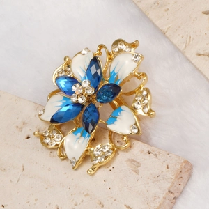 Detail of blue gradient enamel flower brooch with rhinestones on stone background