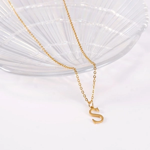 Detailed close-up of capital letter S pendant on a gold chain over glass surface