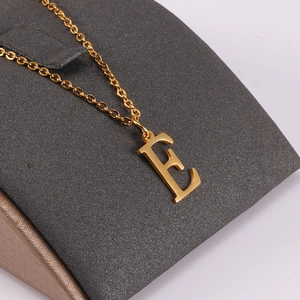 Macro shot of gold-plated stainless steel necklace featuring a polished letter E pendant