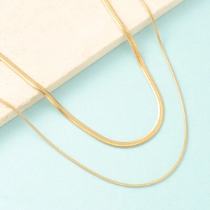 Detailed macro view of layered gold flat snake and thin round chain necklaces on stone