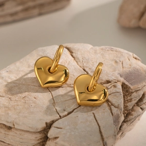 Modern 18K gold plated heart charm hoop earrings displayed on a textured stone surface