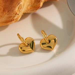 Detailed view of polished golden heart-shaped hoop earrings on a white ceramic plate