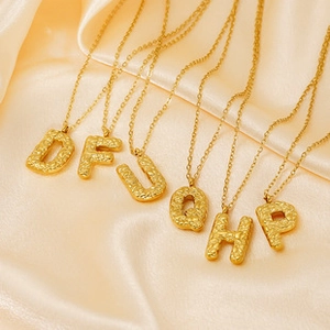 Close-up of golden stainless steel initial lock necklaces with hammered texture on silk