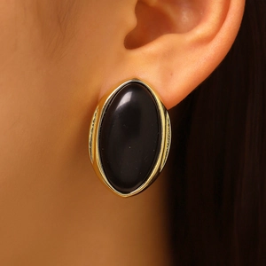 Close-up view of vintage gold-framed oval black resin stud earrings worn on the ear