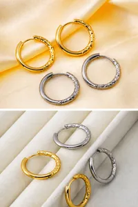 Detail view of gold and silver huggie earrings with hammered metal texture on silk background