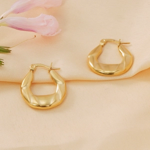 Macro detail of gold-plated hoop earrings with textured matte finish on pink silk fabric