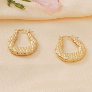 Detailed view of gold snake texture teardrop earrings on a soft pink floral background