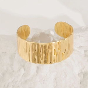 Macro detail of gold-plated open cuff bracelet with hammered bark texture on white stone