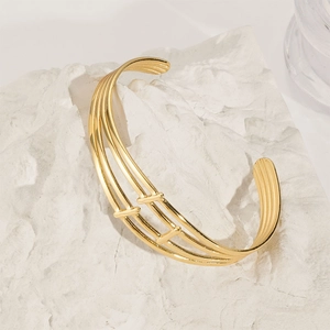 Detail of a gold-plated multi-layer open cuff bracelet on white textured stone