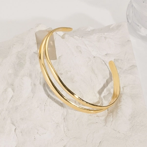 Detail of a minimalist gold-plated double-layer open bangle on a white stone base