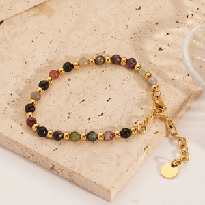 Detail of colorful gemstone beaded bracelet with 18K gold chain on stone plate